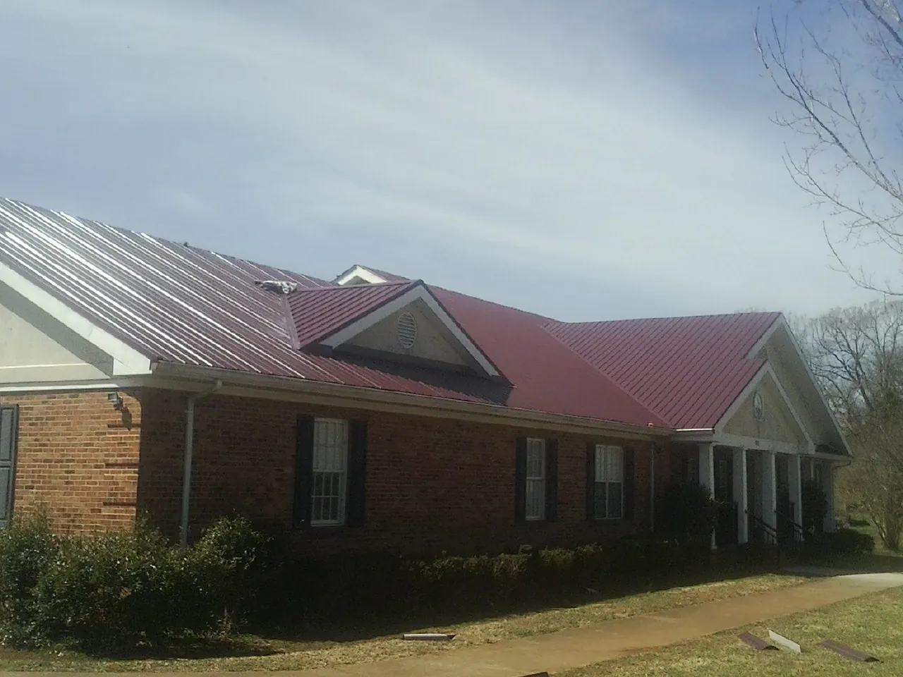 Red metal roof with gabled entries on a long brick building, from a Hail Damage Roof Repair job in Winslow